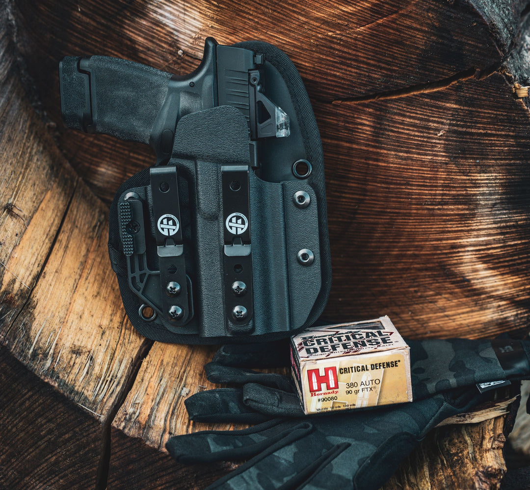 OMNIcarry holster with a micro pistol mossberg mc2 pistol inside  alongside gloves and Hornady Critical Defense ammo on a wood surface.