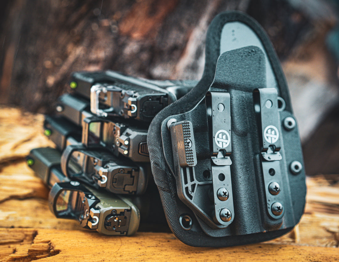 Multi-fit OMNIcarry holster photographed outdoors next to several pistols, highlighting its versatility and custom-like fit